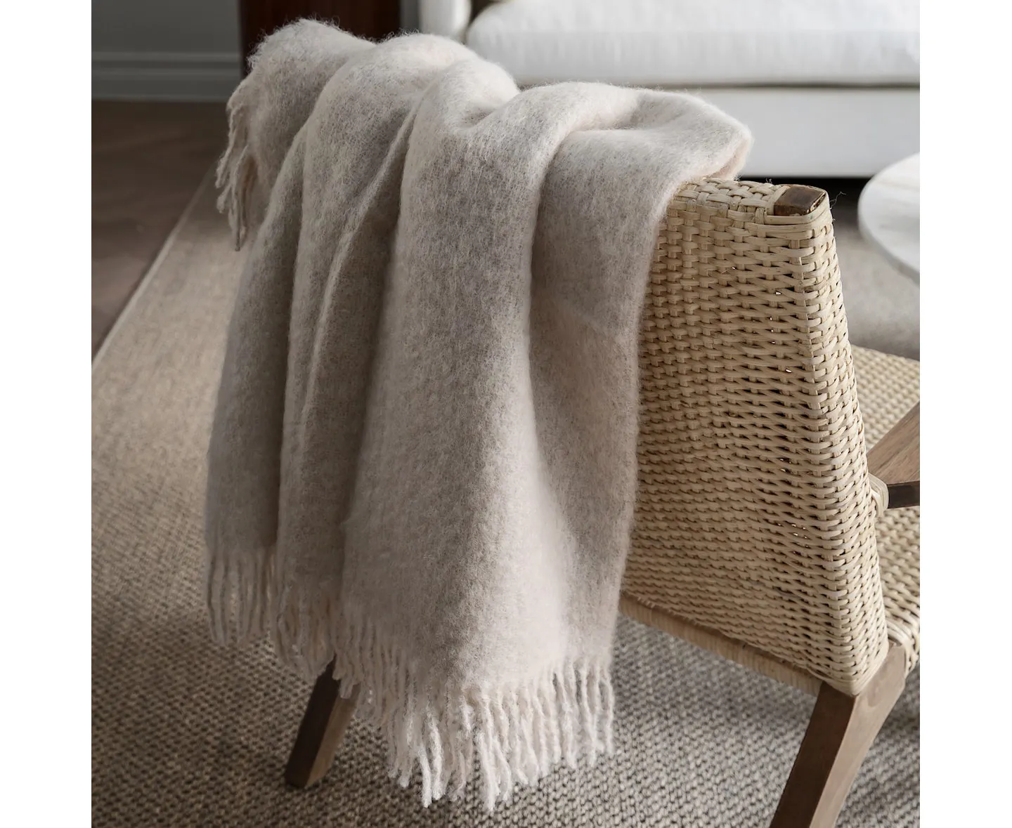 Stackelbergs Mohair Blanket Portabello in Oyster White auf einem Korbsessel