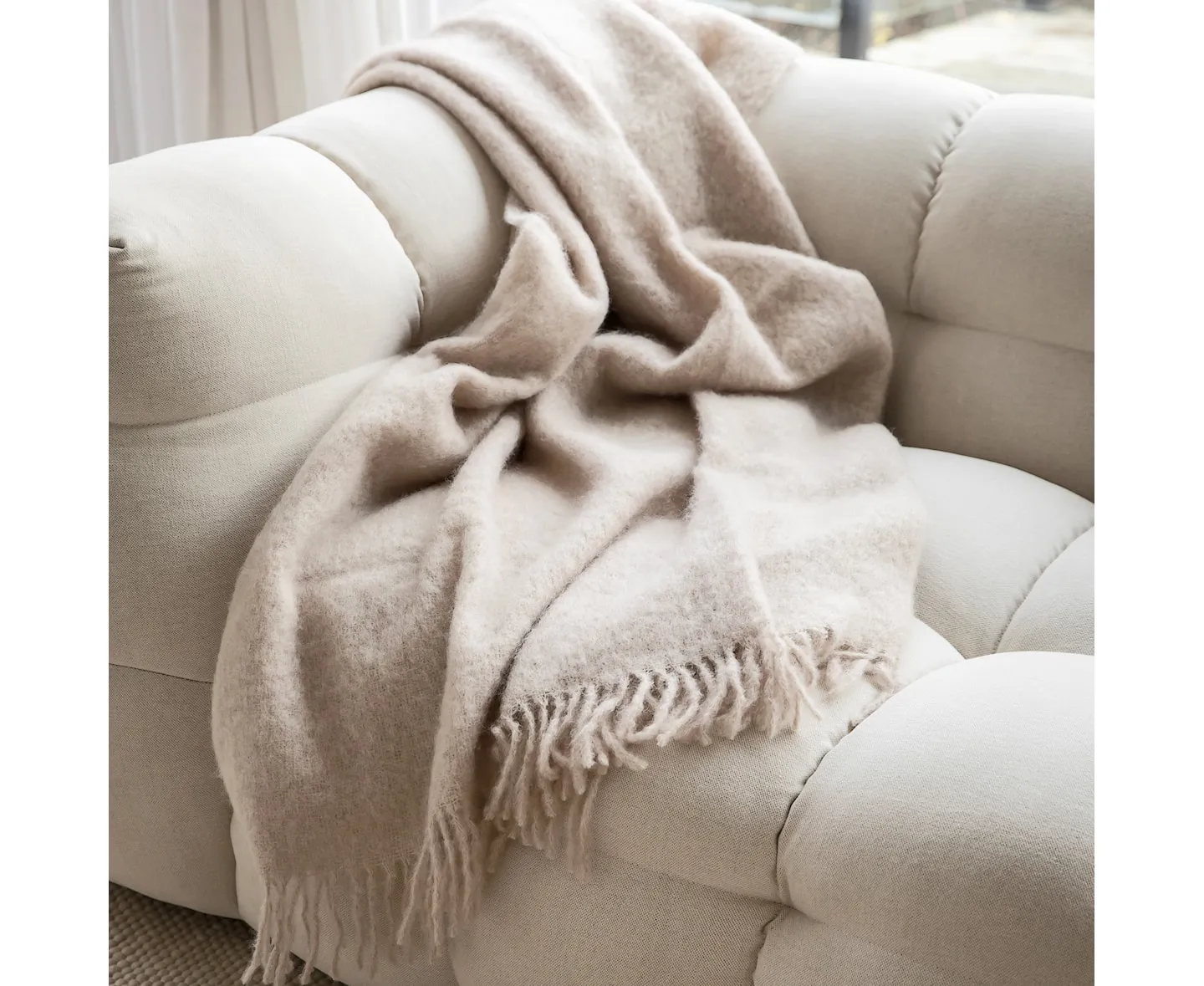 Weiche Mohairdecke Portabello in Oyster White auf einem hellen Sofa